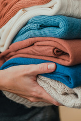 Stack of warm orange and blue pastel sweaters, holding in hands.