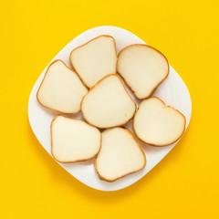 Slices and piece of cheese on plate on yellow colored background, top view