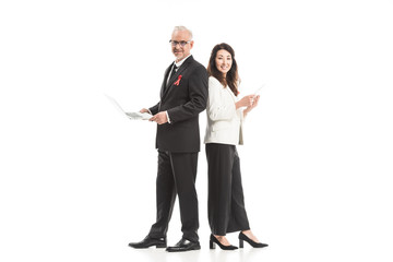 happy adult businesspeople with aids awareness red ribbons working with gadgets while standing back to back and looking at camera isolated on white