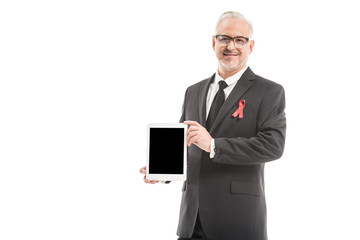 mature businessman in suit with aids awareness red ribbon holding tablet with blank screen isolated on white