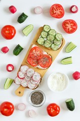 Sandwiches with cream cheese, fresh cucumber, radish, tomato, chia seeds on white background