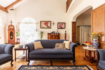 Cobalt blue sofa and other antique furniture on a wooden floor in a spacious living room interior of a classic mansion. - obrazy, fototapety, plakaty