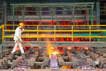 Workers cutting steel ingot behind the continuous casting machine in steel plant