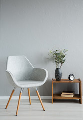 Stylish grey chair next to cabinet with vase and flowers in modern office interior, real photo with...
