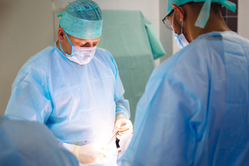 Two male doctors in sterile medical clothes perform an operation in a hospital. Professional team work in a clinic, a surgeon with an assistant. The concept of health, medicine.