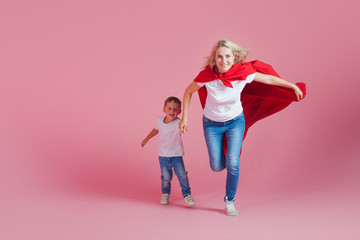 super mom and her son run forward. Fun family, a young blond woman in a red Cape as superhero