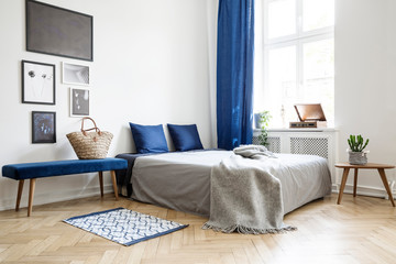 Bedroom design in modern apartment. Bed with dark blue pillows and grey duvet and blanket next to...
