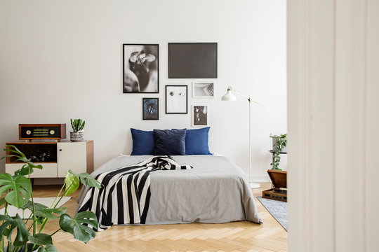 White wooden commode next to bed with dark blue pillows, grey duvet and striped black and white blanket in bedroom with framed art gallery on the wall. Real photo concept