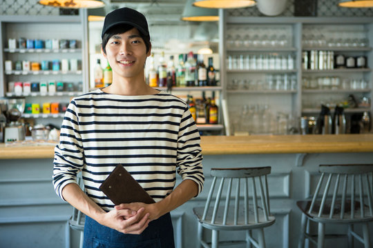 Portrait of smiling barista holding menu in coffee shop