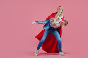 super mom. happy family, a young blond woman in a red Cape and her son jumps and takes off