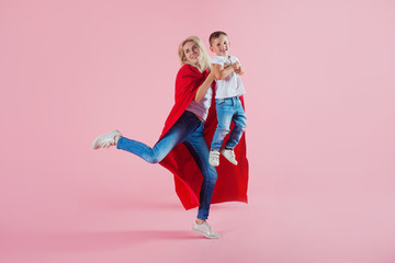 super mom. Fun family, a young blond woman in a red Cape and her son jumps and takes off