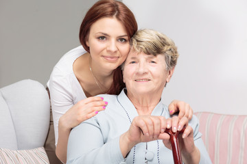 Happy grandmother with walking stick and hugging her smiling daughter
