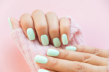 Tender hands with perfect blue manicure on trendy pastel pink background. Place for tex