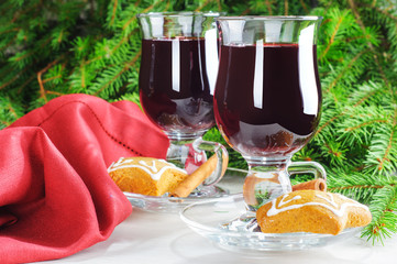 Mulled wine with cinnamon sticks in glass and cookies on the wooden table with christmas tree branch on background
