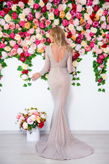 back view of beautiful blond girl in dress posing over colorful flowers background