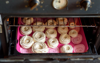 White tasty meringue nests baking in oven
