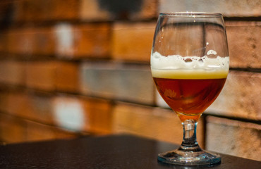 Close up on a glass of amber Pale Ale beer on wooden table in bar on brick wall background with copy space.