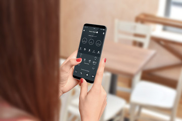 Female person using phone app to control home temperature and security, blurred home interior in background