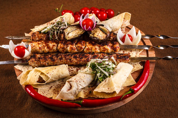 Kebab on skewers on a wooden tray with cherry tomatoes and hot pepper