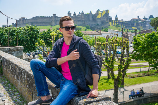 A young man with backpack sits of a view of the castle of Carcassonne in France.