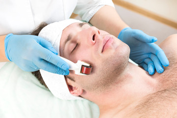 The man undergoes the procedure of medical micro needle therapy with a modern medical instrument derma roller. 