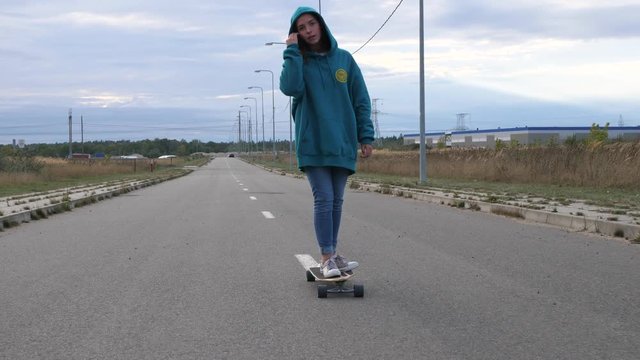 attractive stylish young woman with a hoodie, riding empty road with long board 