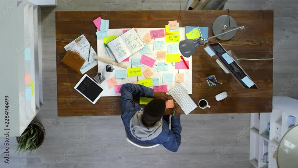 Poster top view of creative young entrepreneur using desktop computer and writing messages on sticky notes,