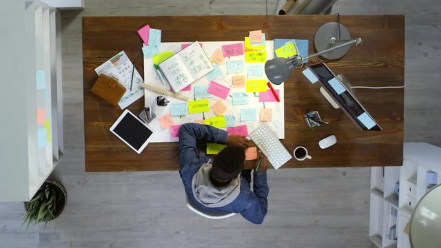 Top view of creative young entrepreneur using desktop computer and writing messages on sticky notes, timelapse