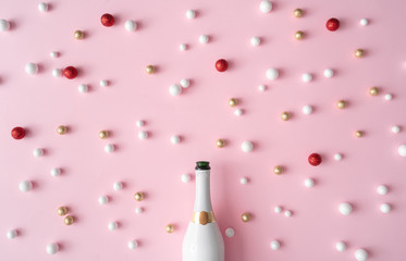 Champagne bottle with red, gold and white glitter decoration balls. New Year greeting card party pink background. Minimal style. Flat lay composition.