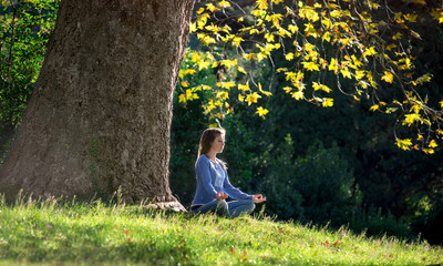 Girl meditates sitting on the grass under a maple tree in autumn