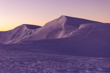 Amazing sunrise in the mountains in winter. Snow-covered peaks of mountains in the rays of the sunrise in the winter frosty morning.