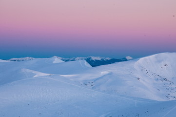 Amazing sunrise in the mountains in winter. Snow-covered peaks of mountains in the rays of the sunrise in the winter frosty morning.