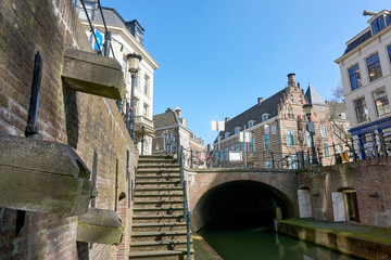 Fototapeta na wymiar Low view on historic street in Utrecht The Netherlands with houses, canal, arch, bridge and staircase against a blue sky