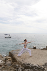 Young woman practicing stretching yoga positions on the seaside, wellbeing and self care concept