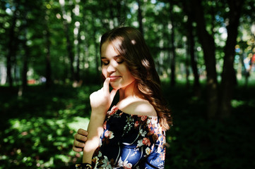 Fototapeta premium Portrait of a fabulous young girl in pretty dress with stylish curly hairstyle posing in the forest or park.