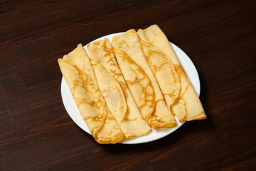 Crepe closeup, heap of thin pancakes on a dish, wood background