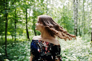 Portrait of a fabulous young girl in pretty dress with stylish curly hairstyle posing in the forest or park.