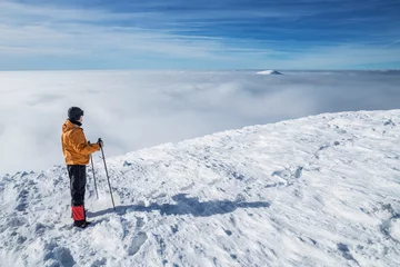 Fotobehang Winter hiking. Tourist on snowy mountain top enjoying beautiful view of cloudscape. © volff