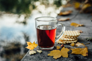 A mug of tea and waffles in the garden with autumn leaves near the water