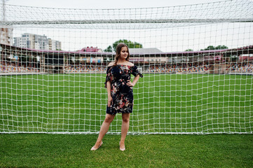 Portrait of a fabulous girl in dress and high heels next to the soccer gates in the stadium.
