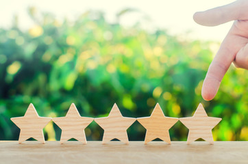 Obraz premium hand points to the fifth wooden star. Get the fifth star. The concept of the rating of hotels and restaurants, the evaluation of critics and visitors. Quality level, good service. selective focus