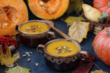 Pumpkin soup in plates against a dark background. Autumn composition. Two plates of soup.