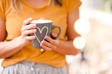 Girl with cup of tea over Christmas lights at background. Coziness. Winter season. Selective focus.