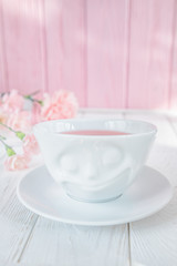 Obraz na płótnie Canvas Fruit tea in white cup and pink carnation flowers on a white background. Free space