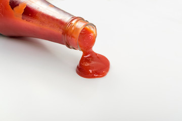 Tomato sauce is poured from the glass bottle on white background