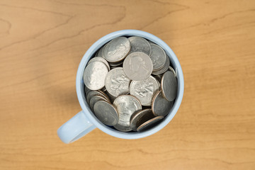 US MONEY QUARTER COINS IN BLUE COFFEE CUP ON WOODEN OFFICE TABLE
