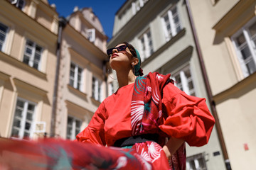 Obraz premium Young spanish woman in a red blouse and green pants. Fashion latin look. Woman walking in old town in Warsaw, Poland