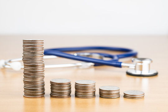 STACKED US QUARTER COINS WITH BLUR BLUE STETHOSCOPE IN BACKGROUND (MEDICATION CONCEPT)