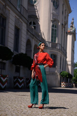 Fototapeta na wymiar Young spanish woman in a red blouse and green pants. Fashion latin look. Woman walking in old town in Warsaw, Poland