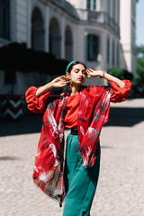 Young spanish woman in a red blouse and green pants. Fashion latin look. Woman walking in old town...